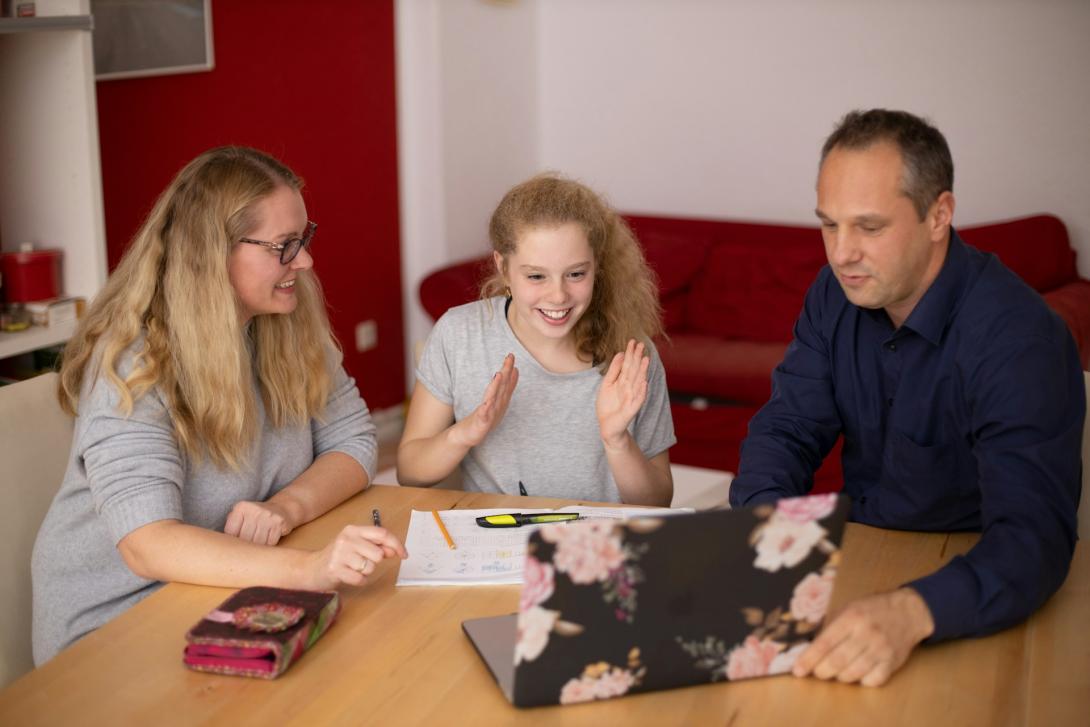zwei Schülerinnen sitzen gemeinsam mit einem Lehrer vor Laptop und Arbeitsmaterialien